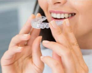 Close-up of a woman holding a clear dental aligner, showcasing dental health and a bright smile.